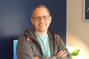 Introducing Creative Director Dom Bartram, a man in glasses standing in front of a computer.